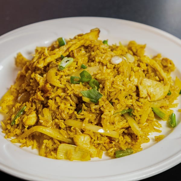 Close-up of golden Thai fried rice with chicken, onions, and green scallions on a white plate.