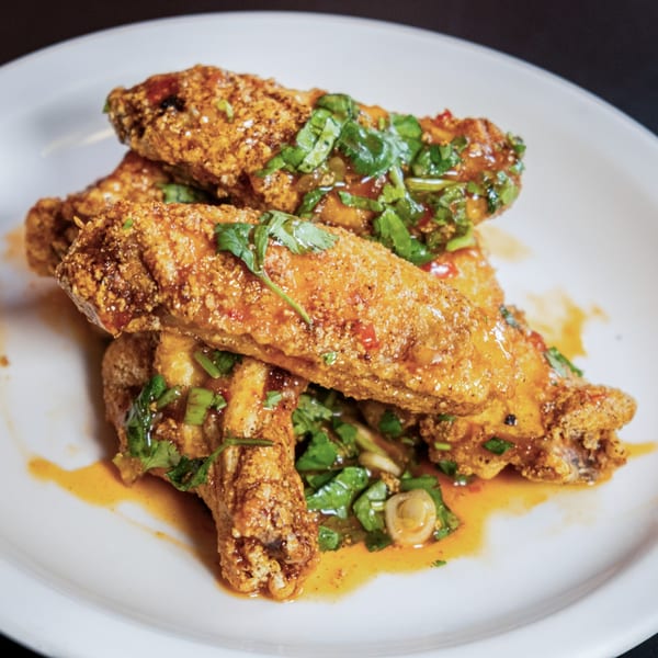 Crispy fried Thai chicken wings, glazed with sauce and garnished with fresh cilantro on a white plate.