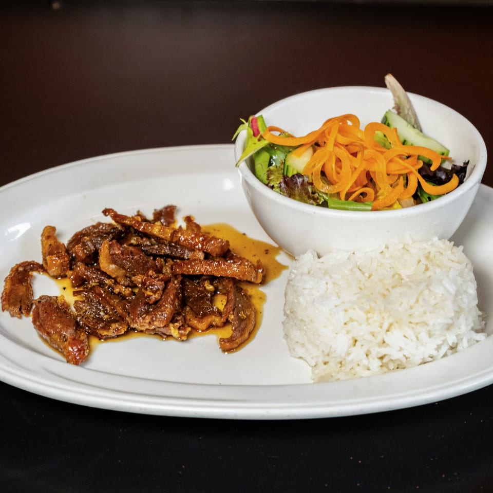 Lily Thai's beef dish with rice and a side salad on a white oval plate.