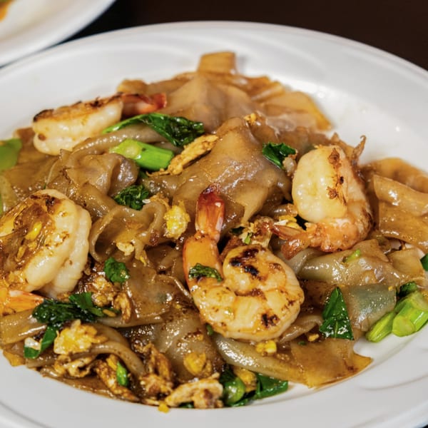 Close-up of Pad See Ew with wide rice noodles, grilled shrimp, egg, and green vegetables.
