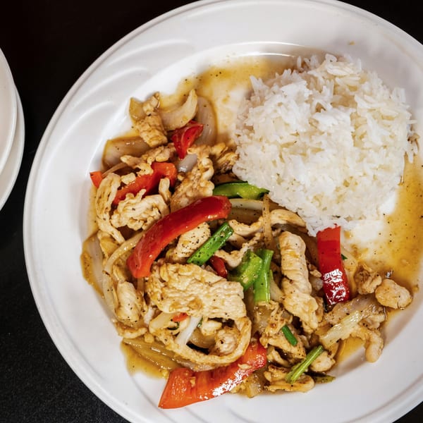 A white plate with stir-fried chicken, red and green peppers, onions, and white rice.