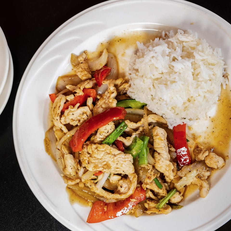 A white plate with stir-fried chicken, red and green peppers, onions, and white rice.