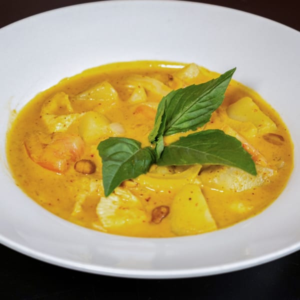 Close-up of a vibrant yellow Thai curry with chicken, potatoes, and basil in a white bowl.