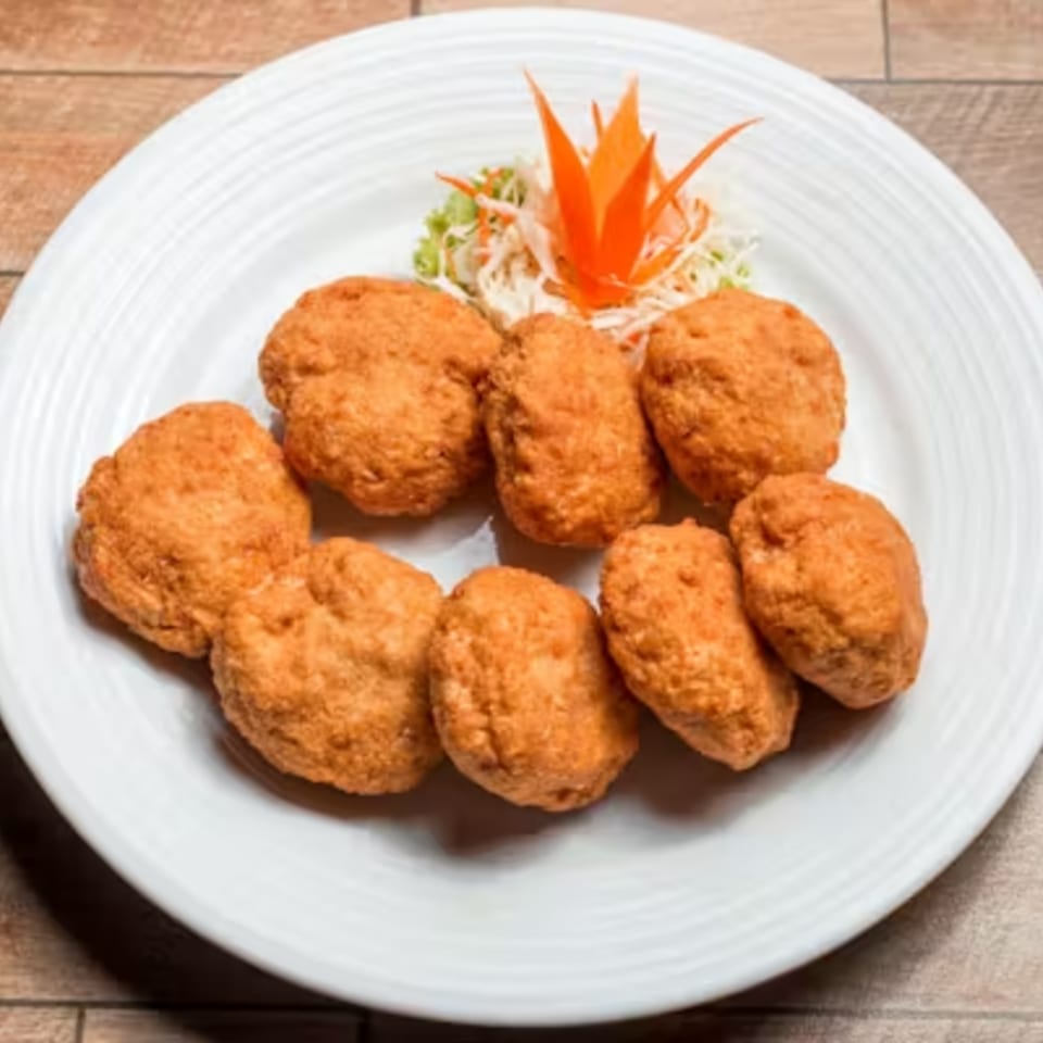Golden-brown fried chicken nuggets on a white plate, garnished with shredded carrots and lettuce.