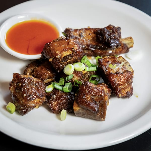 Glazed pork ribs with chopped green onions and a side of red dipping sauce on a white plate.