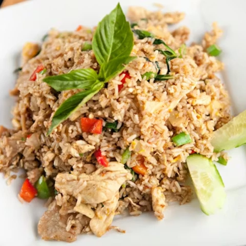 Thai fried rice with chicken, red peppers, green onions, and basil on a white plate.