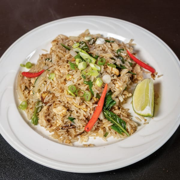 Fried rice with chicken, green onions, red chili peppers, and a lime wedge on a white plate.