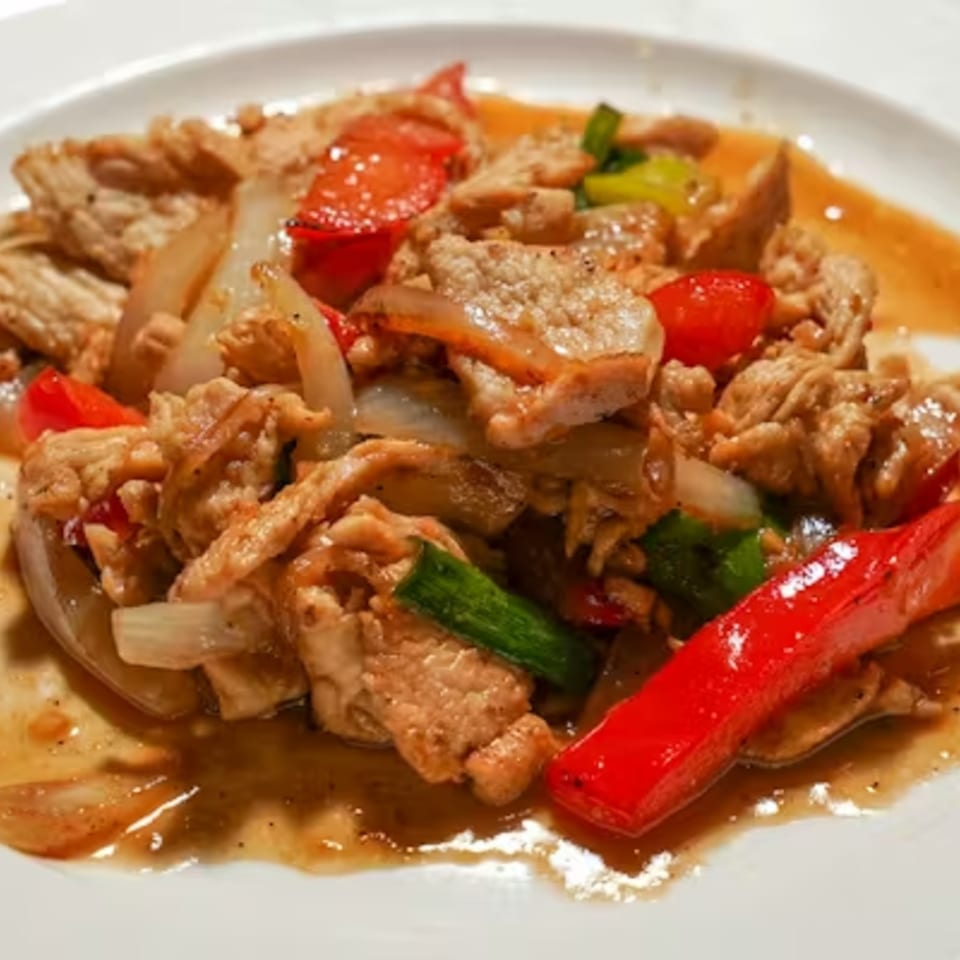 Close-up of a Thai dish with sliced meat, red peppers, onions, and green vegetables in sauce.